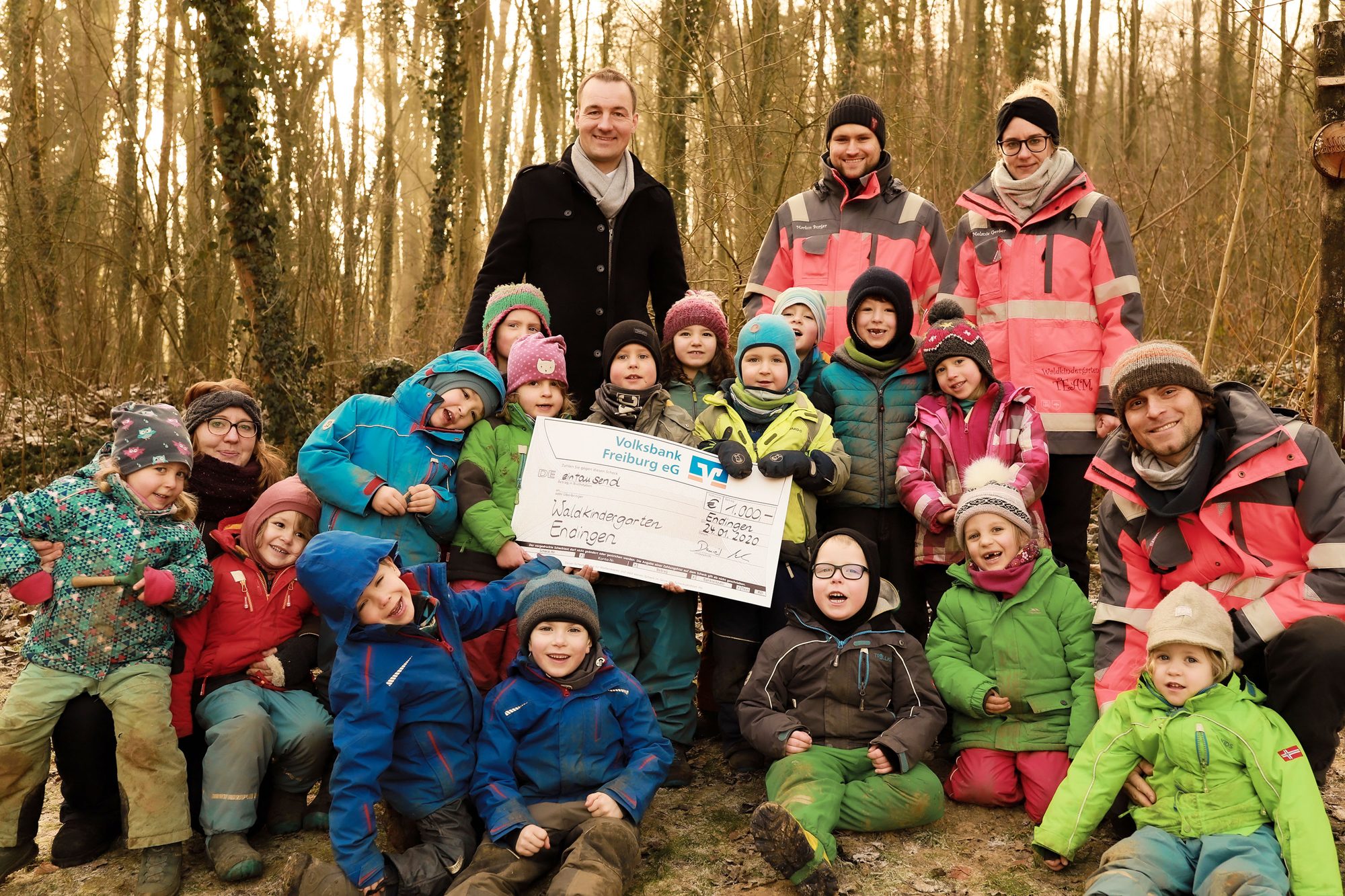 Kindergruppe und Erwachsene im Wald mit Spendenscheck der Volksbank Freiburg