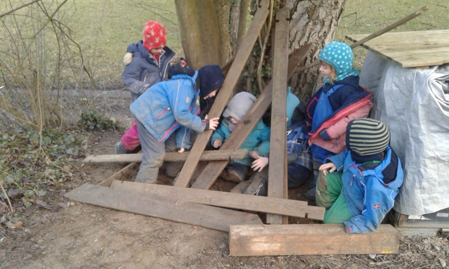 Kinder bauen im Winter mit alten Brettern eine Höhle am Baumstamm