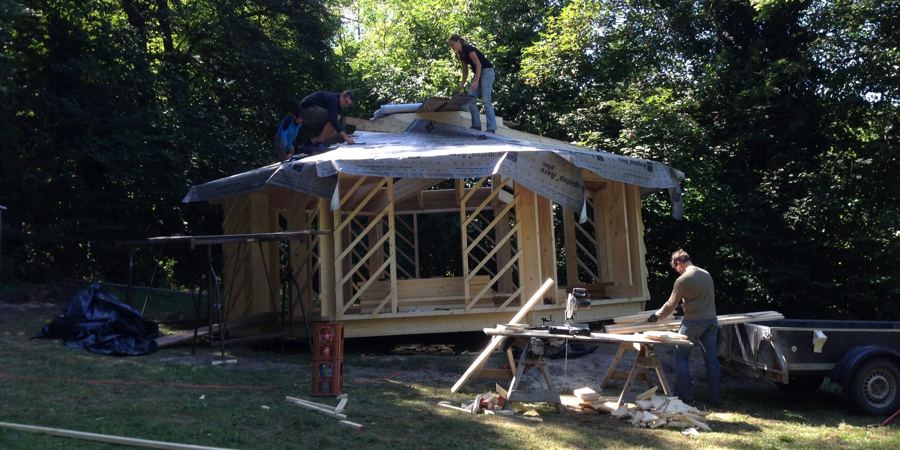 Helfer bauen das Holzgerüst der achteckigen Hütte mit Dachfolie im Wald